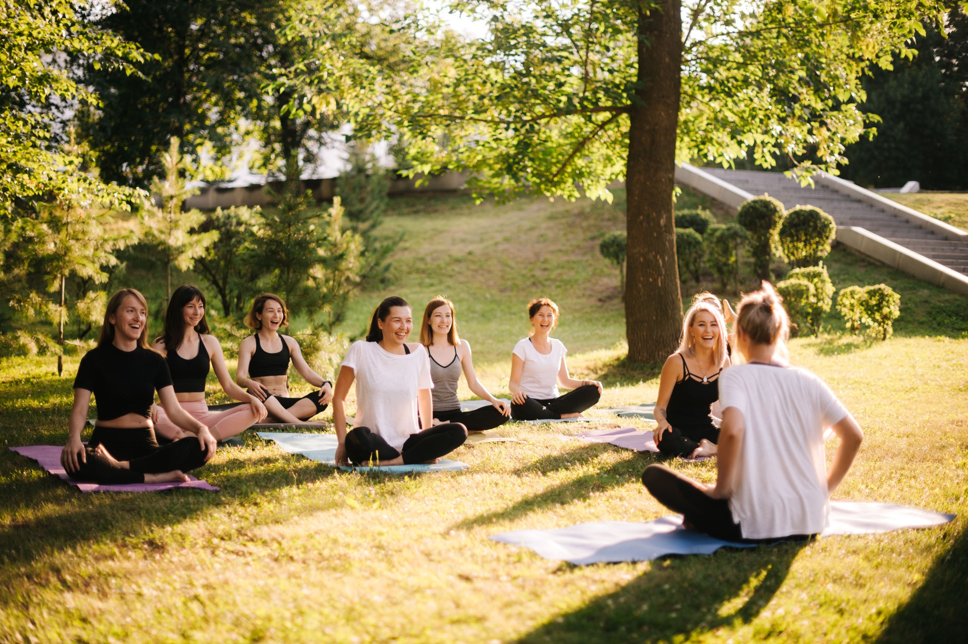 Group of smiling women prepare to meditation in park on summer sunny morning